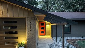 Une maison moderne avec une porte de garage, une porte rouge et une entrée bien éclairée.