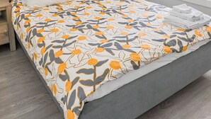 Una cama bien hecha con colcha estampada de flores, una mesita de noche y una ventana con persianas.
