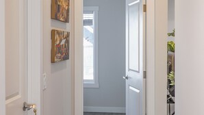 Un pasillo con paredes blancas, suelo de madera y dos puertas que dan a otras habitaciones.