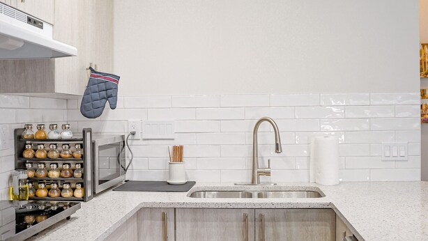 Una cocina moderna con alacenas de madera clara, un lavamanos de acero inoxidable y un microondas integrado.