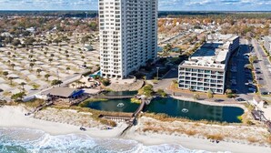 Een hoog hotel met een centrale binnenplaats, een strandgedeelte en een parkeerplaats.
