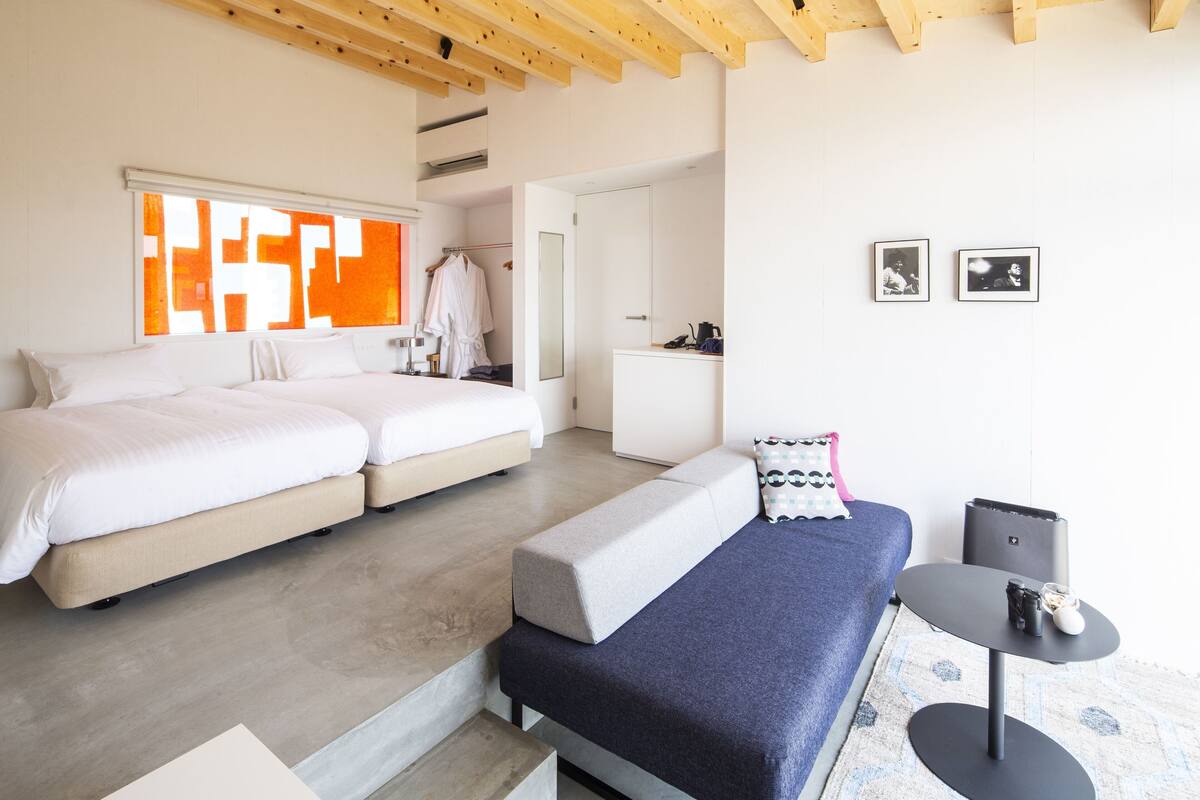 A modern bedroom with a large bed, a smaller bed, a sofa, and a small table.
