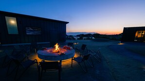 A circular outdoor seating area with a fire pit, surrounded by chairs, in front of a building with a large window and a view of the landscape. - TUZUMI WAKAYAMA SUSAMI (Susami)