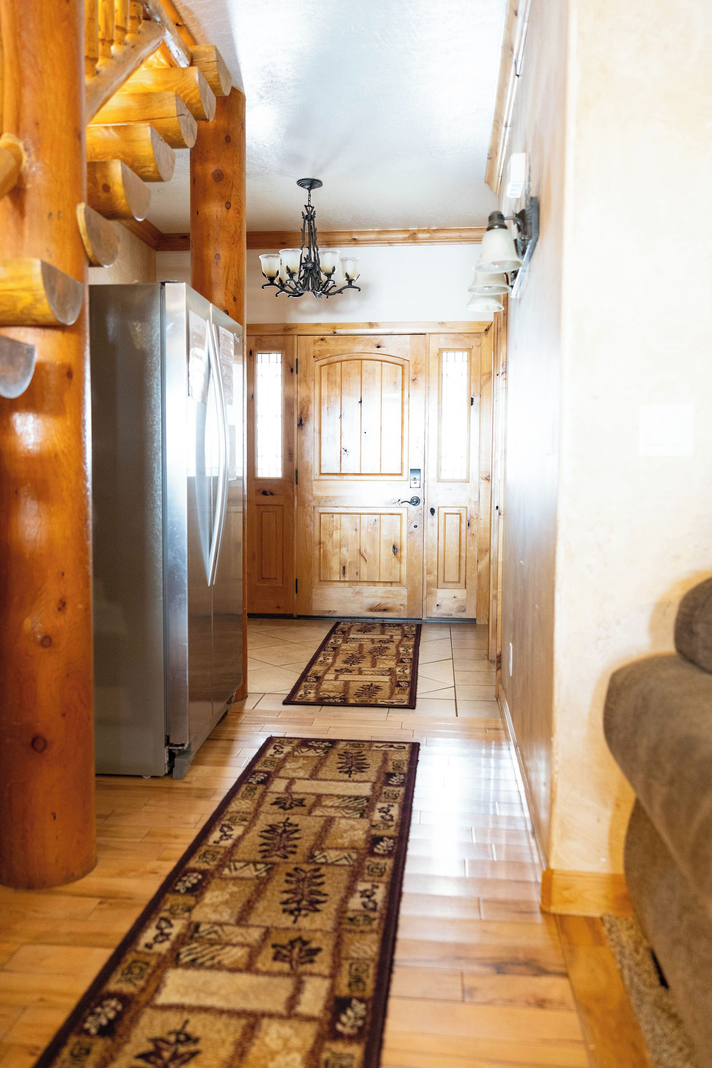 A wooden interior with a refrigerator, a chandelier, and a patterned rug.