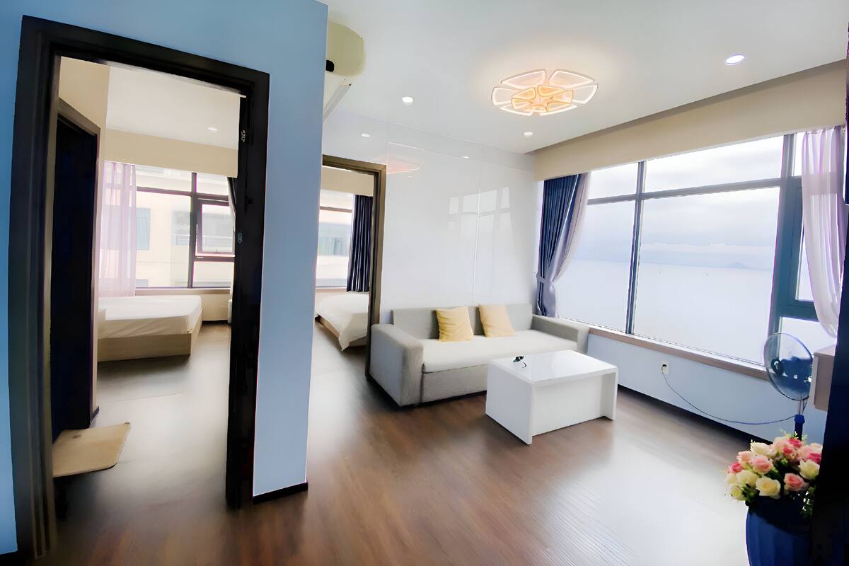 A modern hotel room with a large window, a sofa, a coffee table, and a small side table.