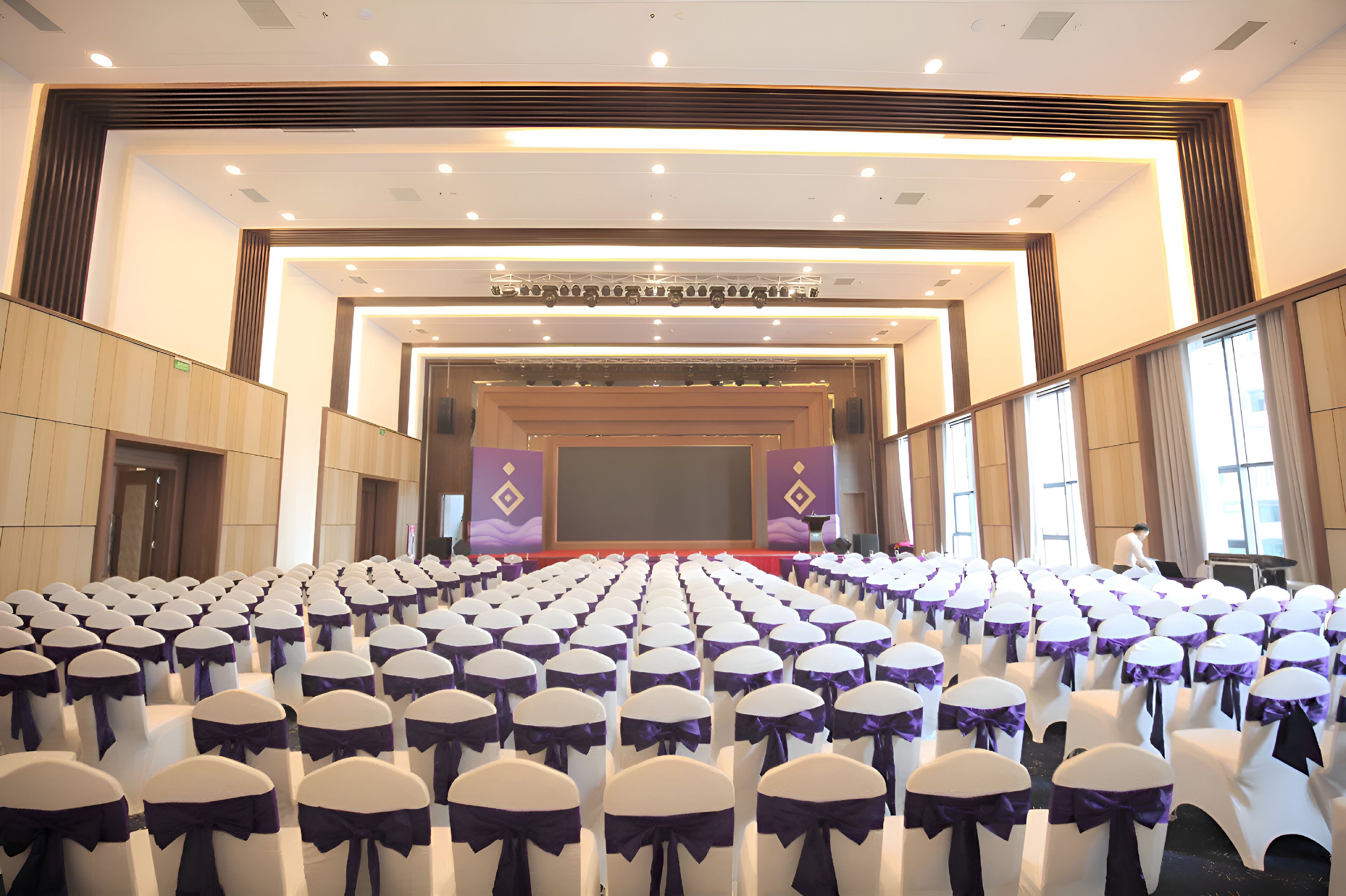 A conference room with rows of white chairs with purple sashes, a stage with a podium, and a large screen.