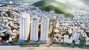 Vista aérea de una ciudad costera con rascacielos, una playa y montañas al fondo.