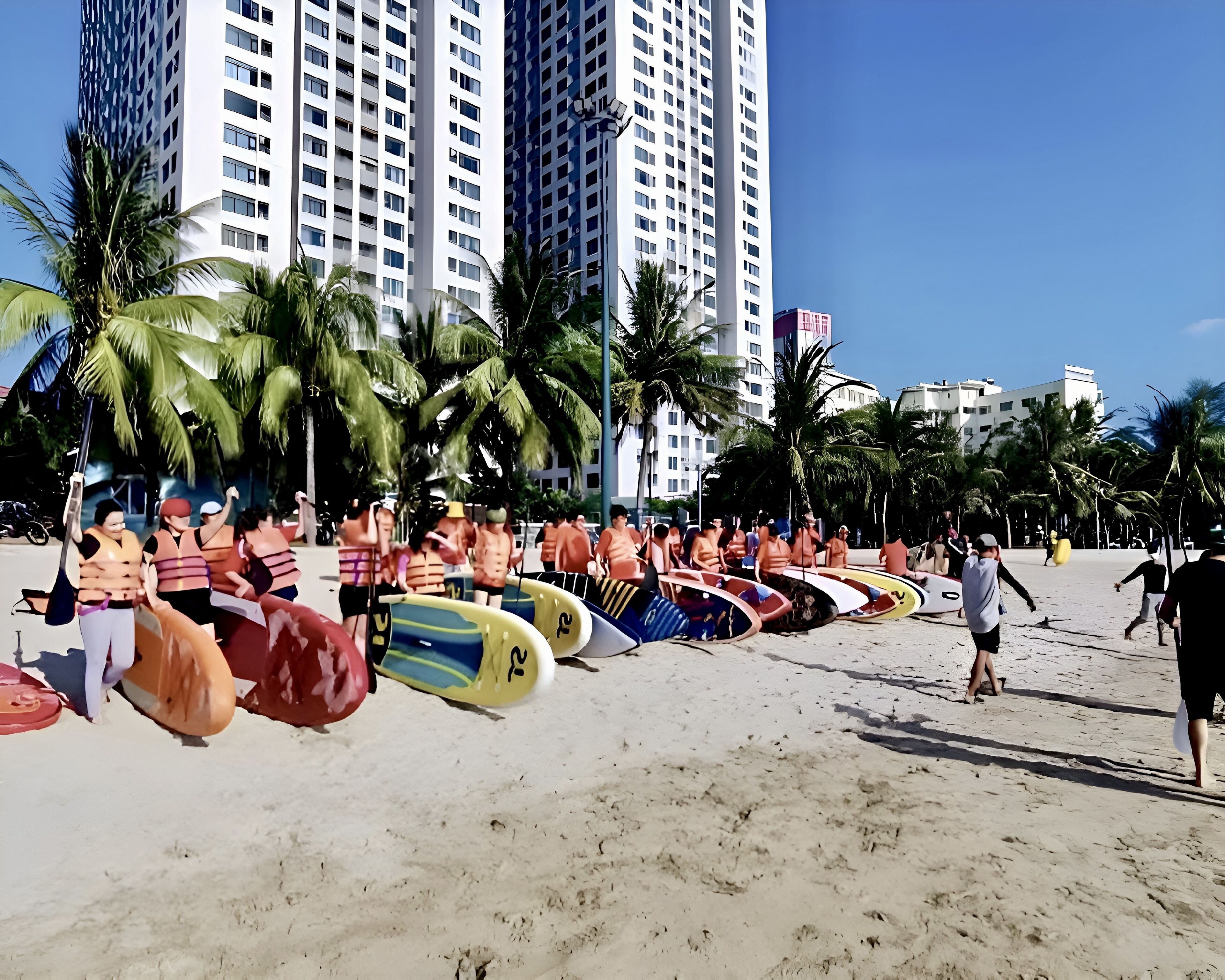 A beach with surfboards lined up and people in orange life vests.