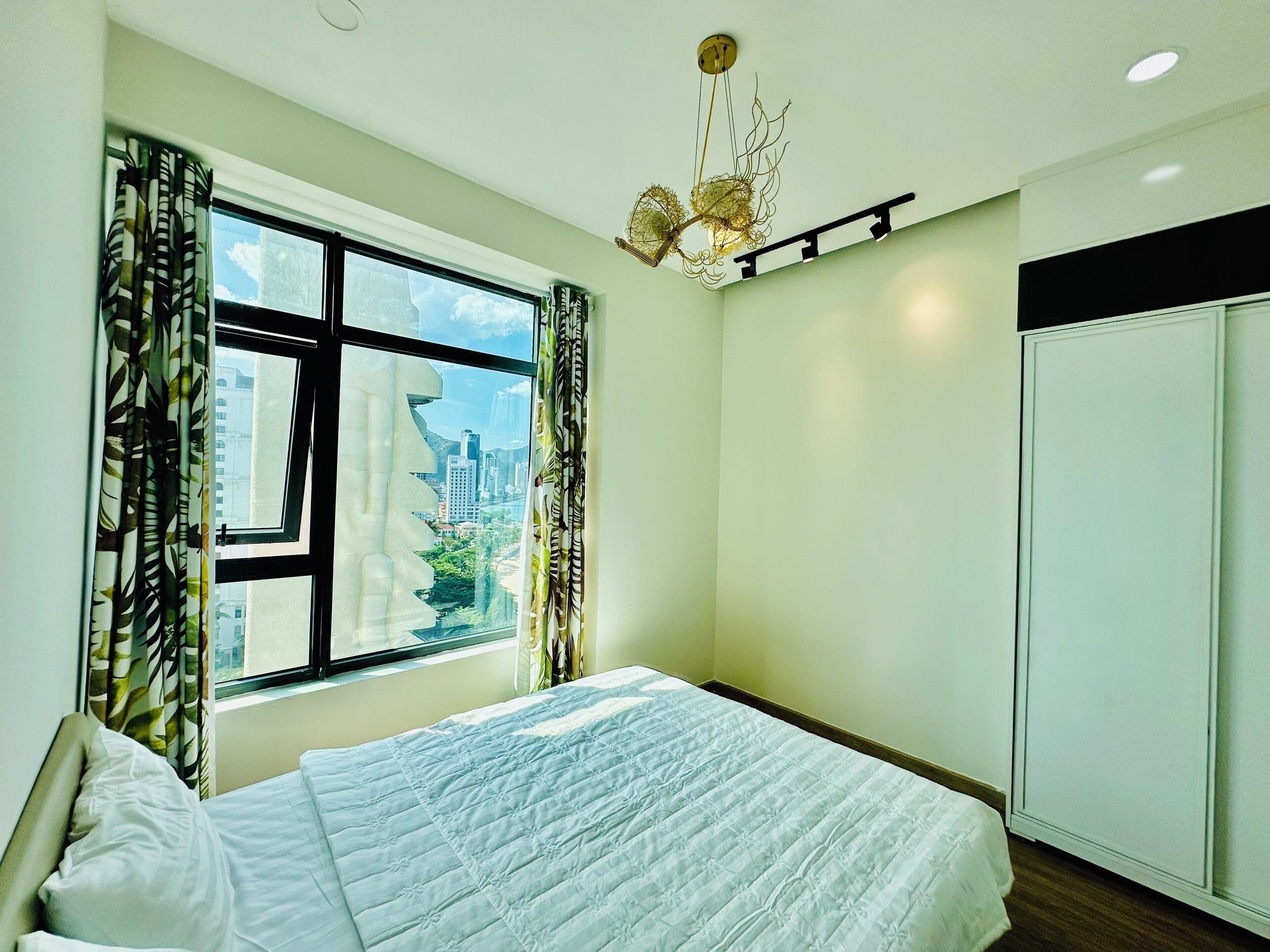 A bedroom with a bed, a window with curtains, a chandelier, and a wardrobe.