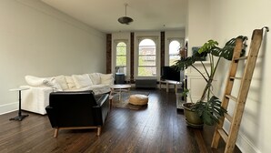 A spacious living room with a white sofa, a black armchair, a wooden floor, and a large potted plant.