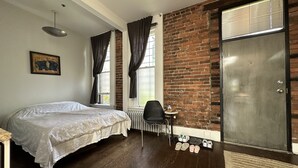 A bedroom with a bed, a chair, a radiator, a shoe rack, and a brick wall.