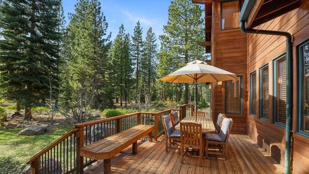 A wooden deck with a table and chairs, surrounded by a railing, overlooking a forested area.