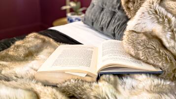 A bed with a fur blanket, an open book, and a bedside lamp.