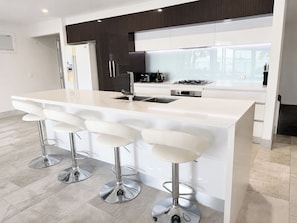 A modern kitchen with a central island, bar stools, stainless steel appliances, and a view to the outside.