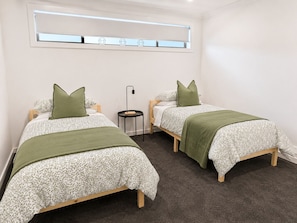 A twin room with two beds, a small table, a lamp, and a window with blinds.