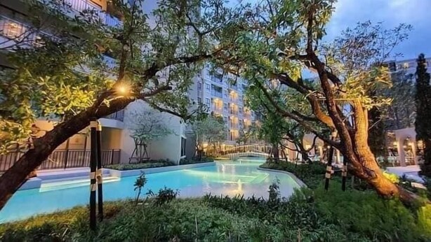 A pool area surrounded by trees and a building with balconies.