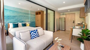 A modern hotel room with a large bed, a sofa, a dining area, and a kitchen.