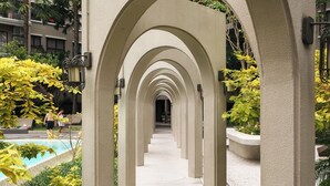 A pathway with multiple arches leading to a pool area, surrounded by greenery and a building in the background.