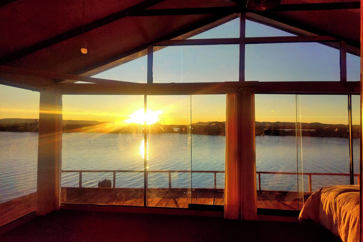 A room with a large window overlooking a body of water during sunset.