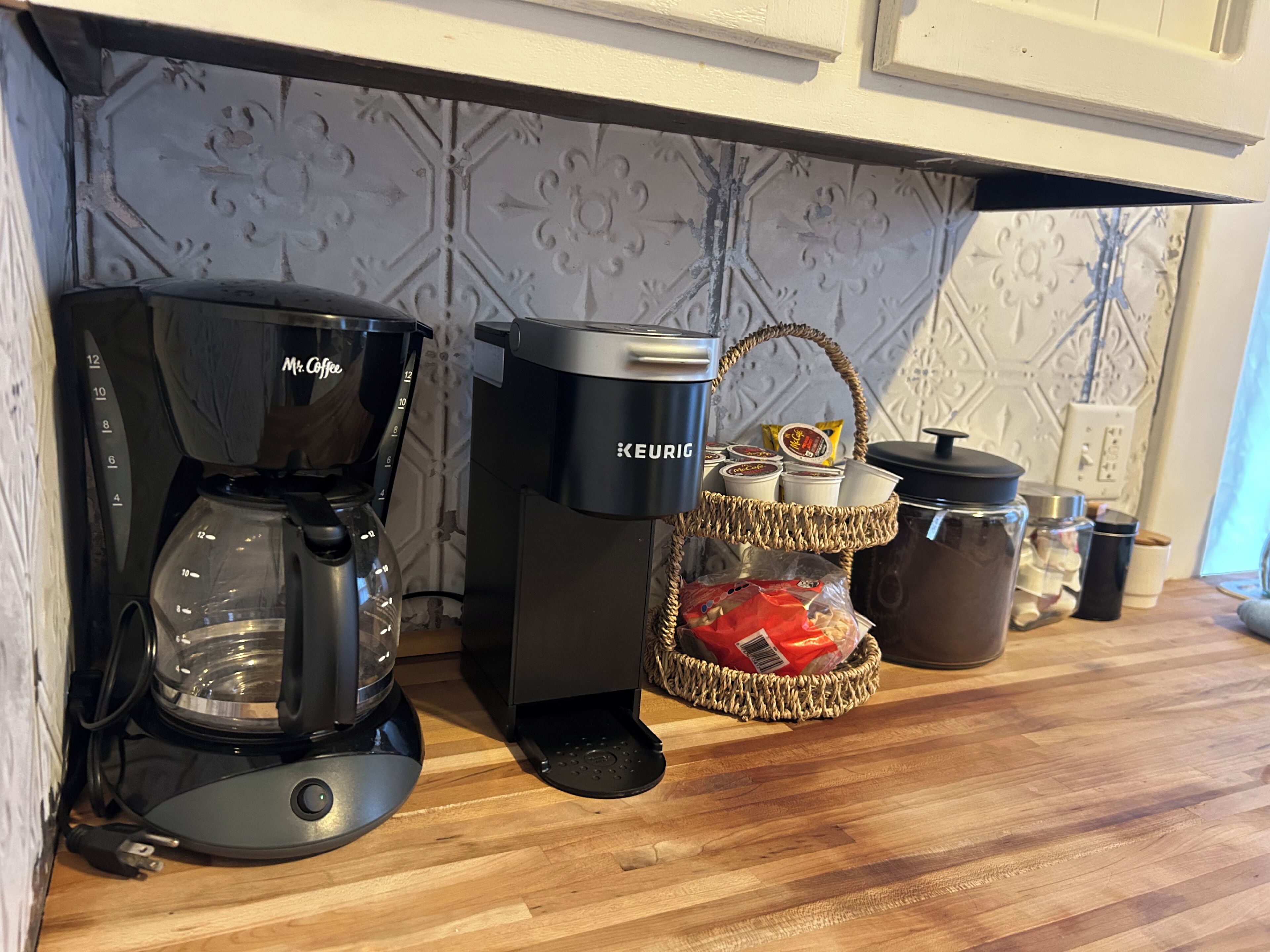 Een koffiezetapparaat, een Keurig, en een mand met snacks op een keukentafel.