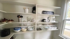 Eine Küche mit weißen Regalen, diversen Küchenutensilien und einem Schild mit der Aufschrift 'kochen, singen, tanzen'.