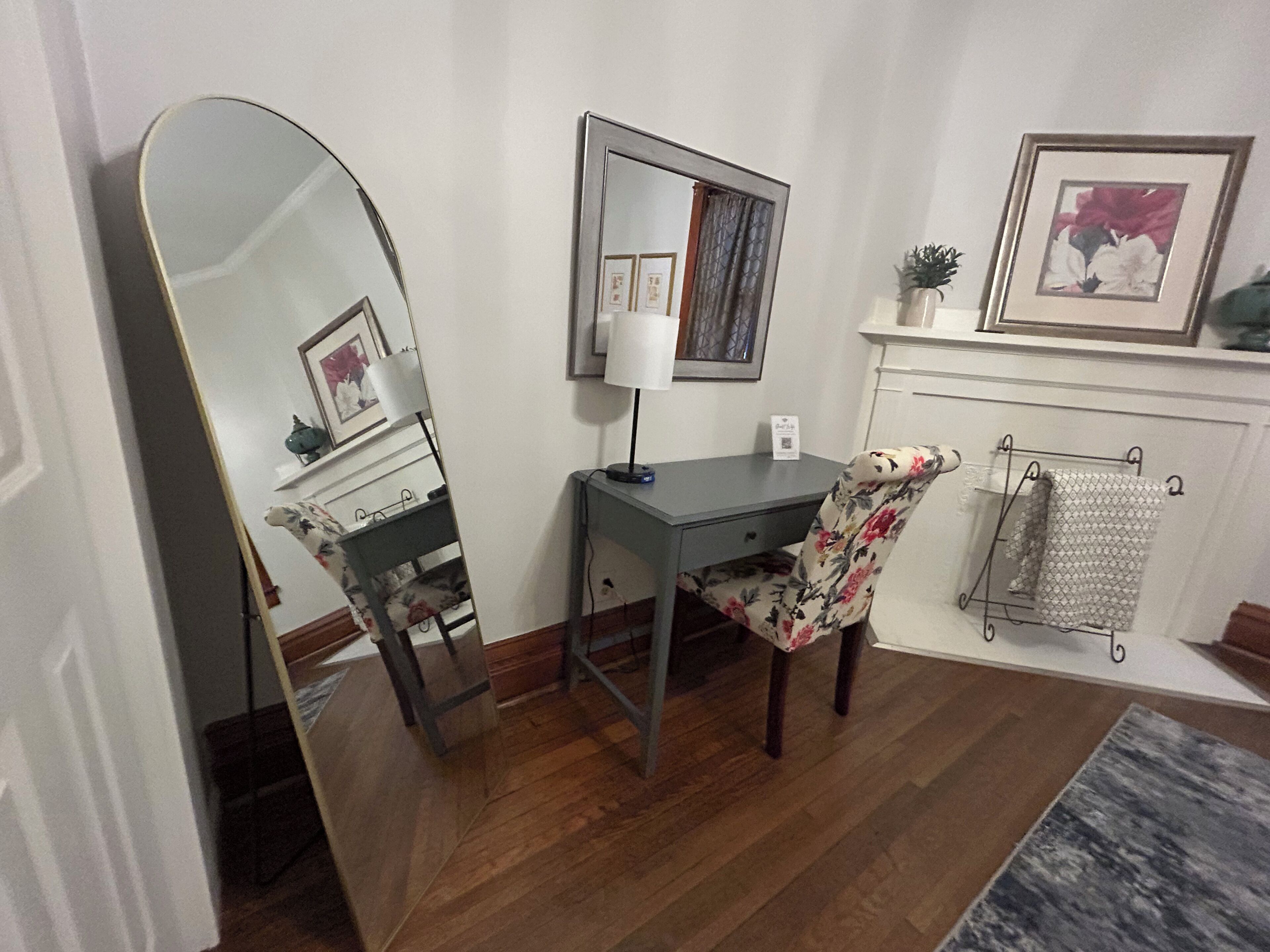 Una habitación con escritorio, silla, espejo grande, lámpara y radiador.