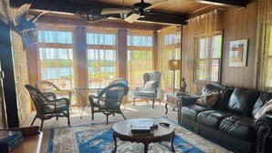 A cozy living room with a leather sofa, two armchairs, a coffee table, and a large window with curtains. - American House 1854- Steamboat Landing, 4 Bedrooms, 1.5 Bath, Full Kitchen (McGregor)