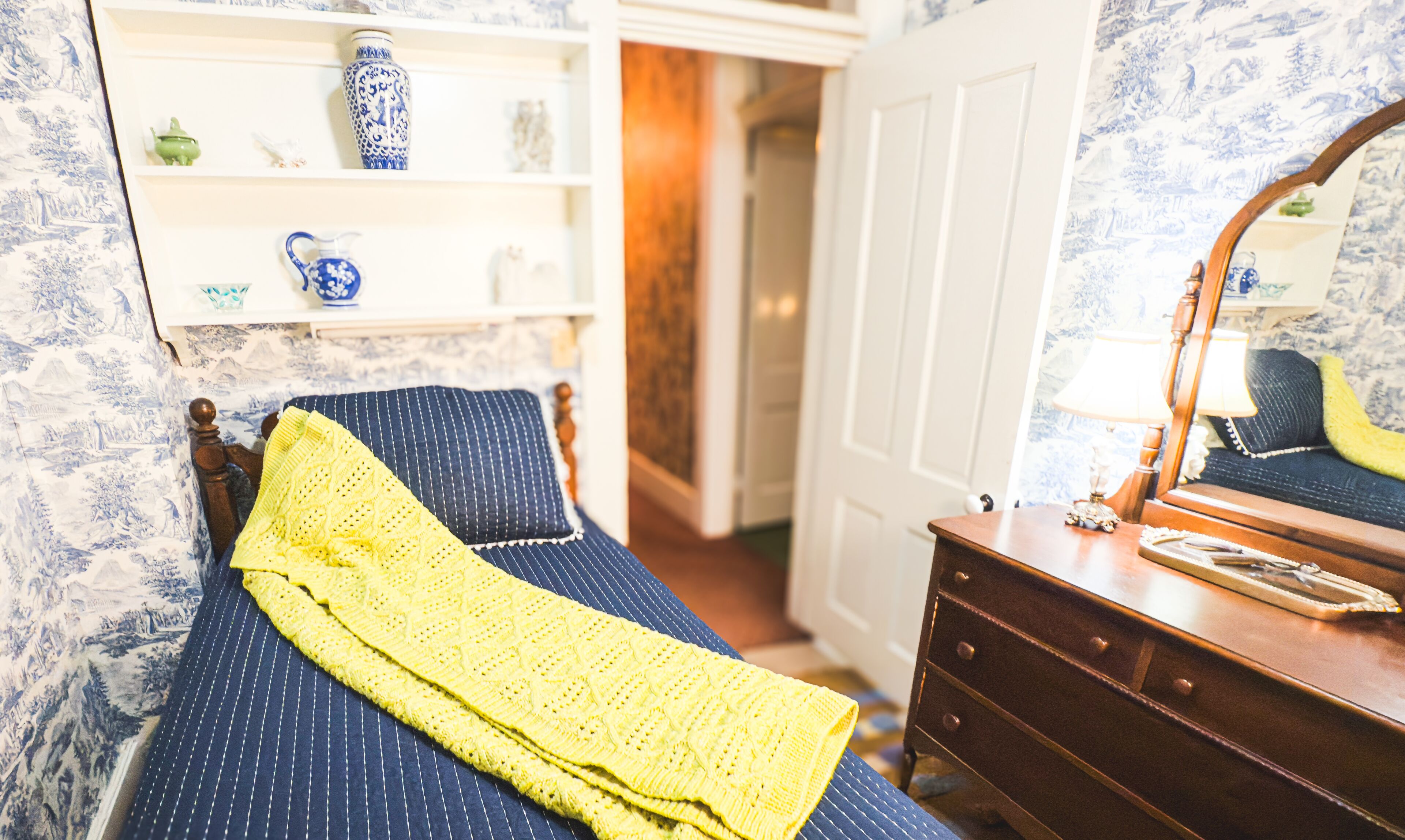 Una habitació amb un llit, un taulell, un mirall i una estant amb objectes decoratius.
