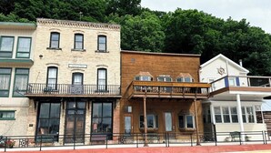 A row of buildings with distinct architectural styles, including a brick building labeled "American House" and a wooden structure with a balcony. - American House 1854- Steamboat Landing, 4 Bedrooms, 1.5 Bath, Full Kitchen (McGregor)