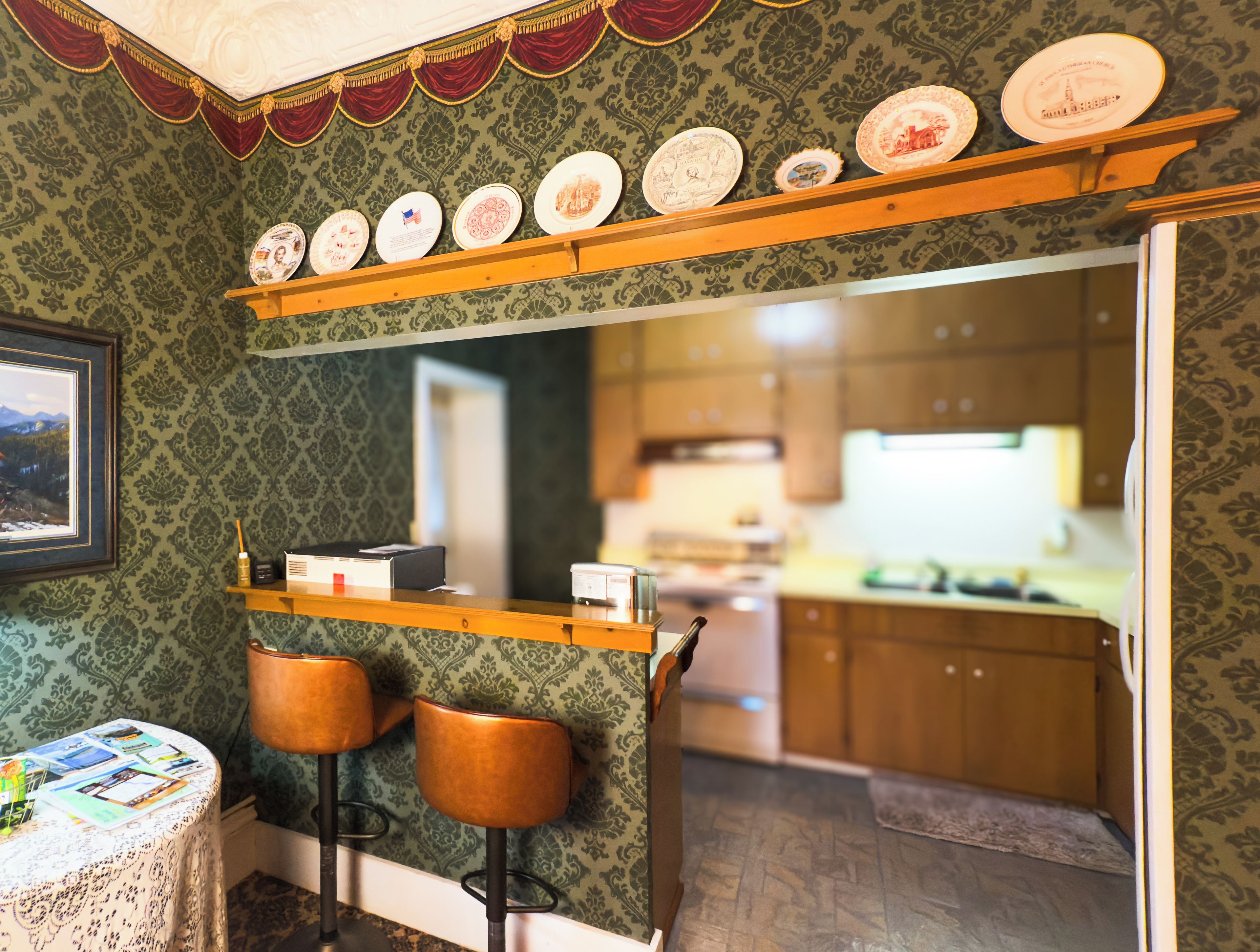 A bar area with stools, a shelf with plates, and a view into a kitchen.