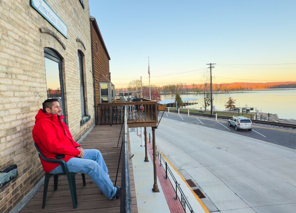 A man sitting on a bench outside a building with a view of a lake and a road.