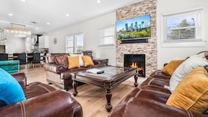 A spacious living room with leather sofas, a glass coffee table, a fireplace, and a cityscape painting.