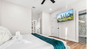 A modern hotel room with a large bed, a cityscape TV, and a marble accent wall.