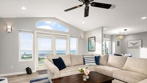 A modern living room with a large sectional sofa, a wooden coffee table, and a ceiling fan. - Perch - La Fiesta 34: Luxe Retreat w/ Serenity View & Firelit Comfort (Coupeville)
