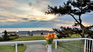 A patio with a table and chairs, a white vase with flowers, and a view of houses and a tree. - Perch - La Fiesta 34: Luxe Retreat w/ Serenity View & Firelit Comfort (Coupeville)