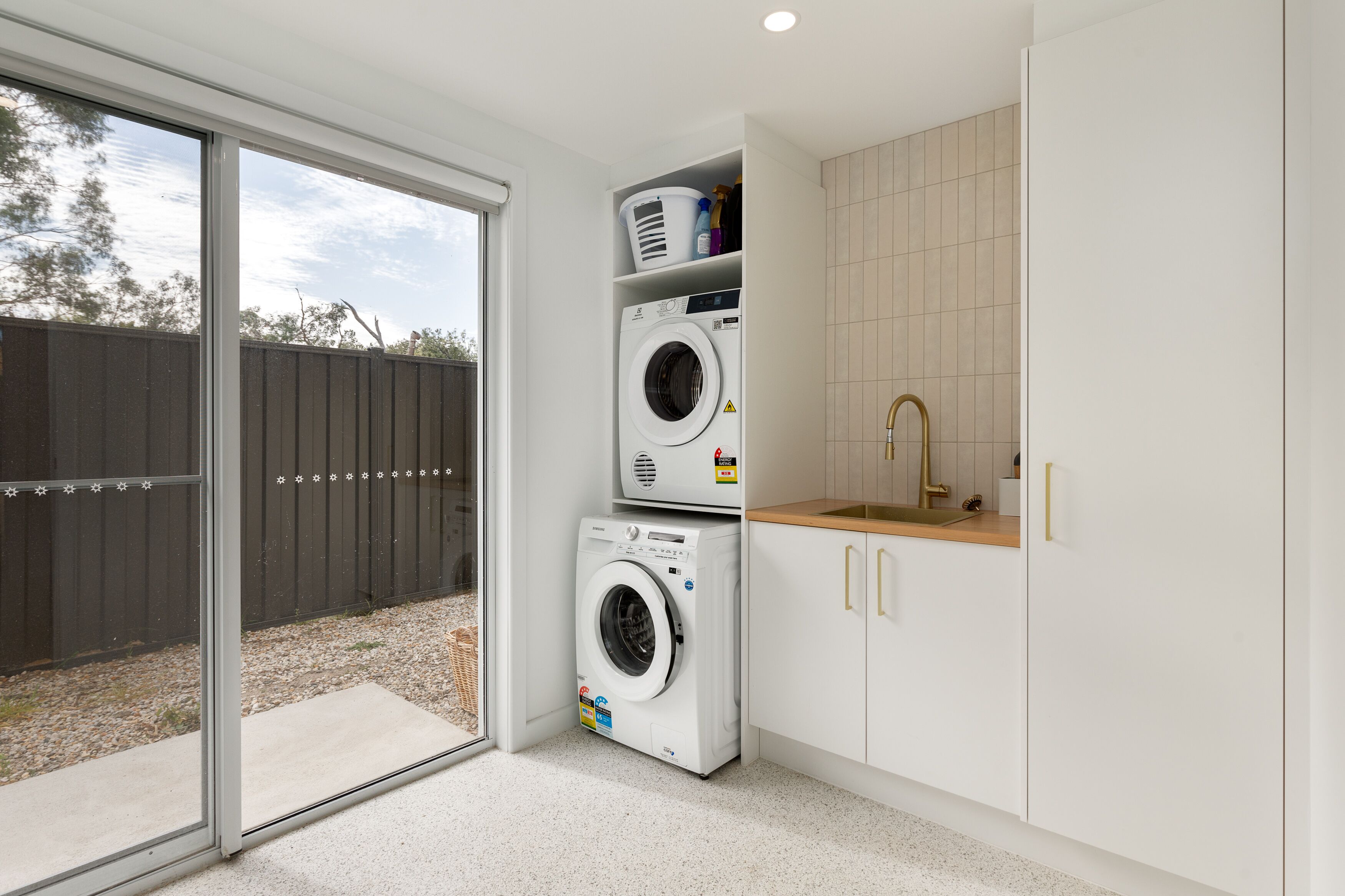 A laundry area with two stacked washing machines, a sink, and a window overlooking a backyard.
