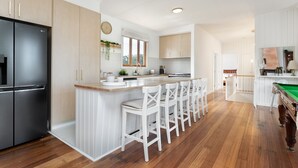 Een moderne keuken met een centraal eiland, witte barstoelen en een pooltafel.