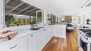 A modern kitchen with white cabinetry, a large island with a sink, and a view of the outdoors. - 'Torrente House' - Berry, NSW (Berry)