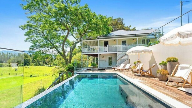 A swimming pool with lounge chairs and umbrellas, surrounded by a lush green landscape and a two-story building with a balcony. - 'Torrente House' - Berry, NSW (Berry)