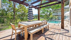 A wooden deck with a table and chairs, overlooking a swimming pool and lush greenery. - 'Torrente House' - Berry, NSW (Berry)