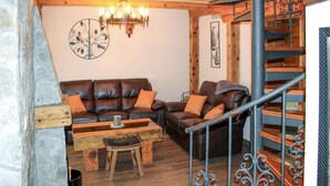 A cozy living room with a leather sofa, wooden coffee table, and a small stool. A chandelier hangs from the ceiling, and a staircase with wrought iron railings is visible. - Nice home in Korenica with sauna (Korenica)