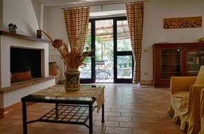 A living room with a fireplace, a table with a vase, a yellow armchair, and a view through a glass door to an outdoor area. - Agriturismo Casa Greppo - Il Noce (San Venanzo)