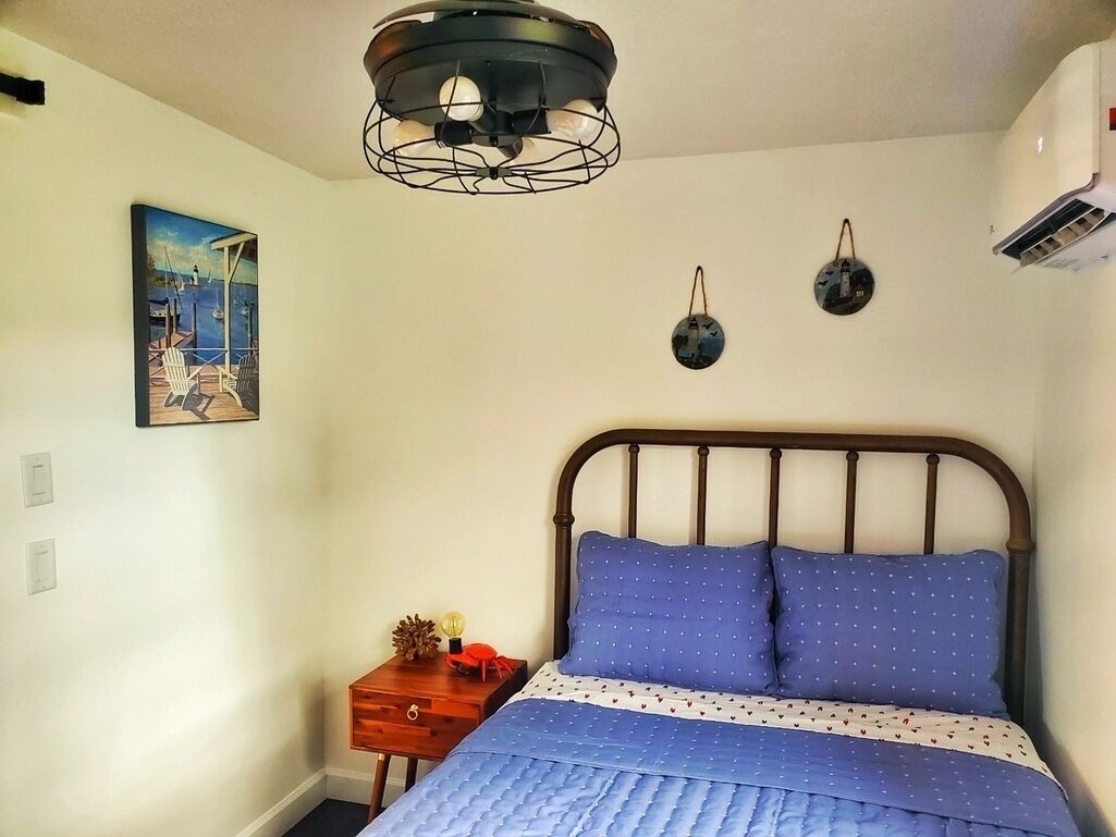 Een slaapkamer met een bed, nachtkastje, schilderij en een lamp.