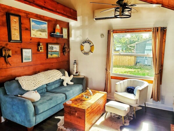 A cozy living room with a blue sofa, a wooden coffee table, and a white armchair. There are framed pictures on the wall, a small lighthouse model, and a "PANAMA CITY" sign. - Captain Cove’s Cottage - Oasis by the Marina (Stuart)