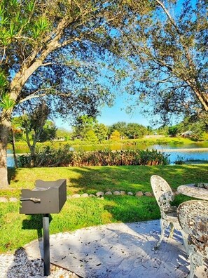 A patio with a grill, outdoor furniture, and a pond in the background. - Captain Cove’s Cottage - Oasis by the Marina (Stuart)