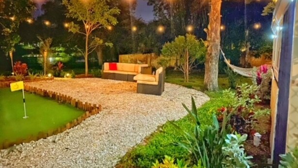 Un espace extérieur aménagé avec des sièges, un green d’entraînement au putting et des guirlandes lumineuses.