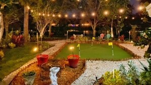 Un jardin illuminé la nuit, avec un green d’entraînement au golf, des guirlandes lumineuses et des plantes en pot.