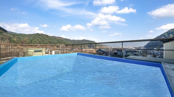 A rooftop swimming pool with a clear view of a mountainous landscape and a town in the background.