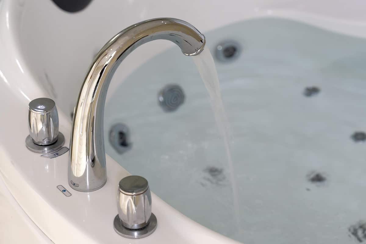 A bathtub with a single chrome faucet and a control knob.