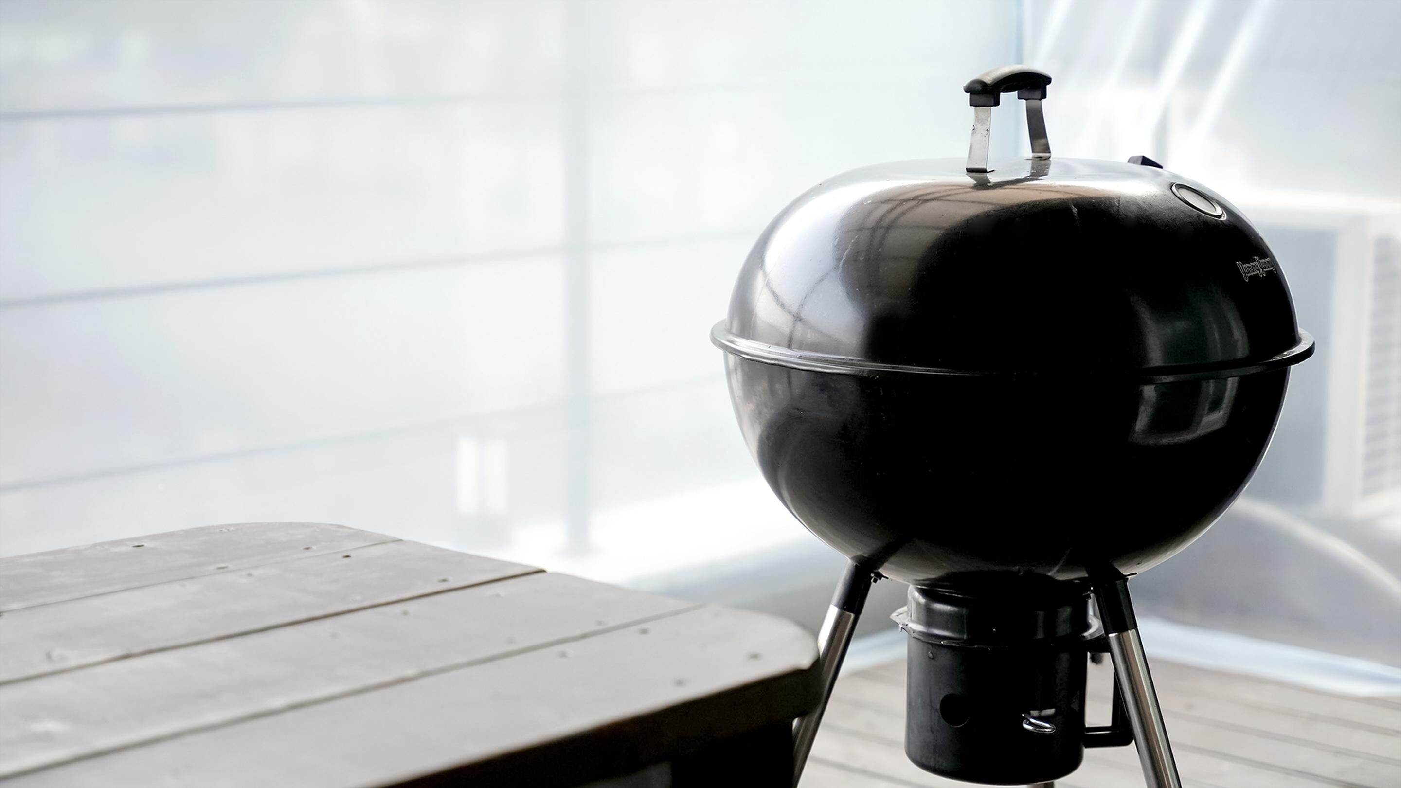 A portable grill on a wooden table in a bright room with large windows.